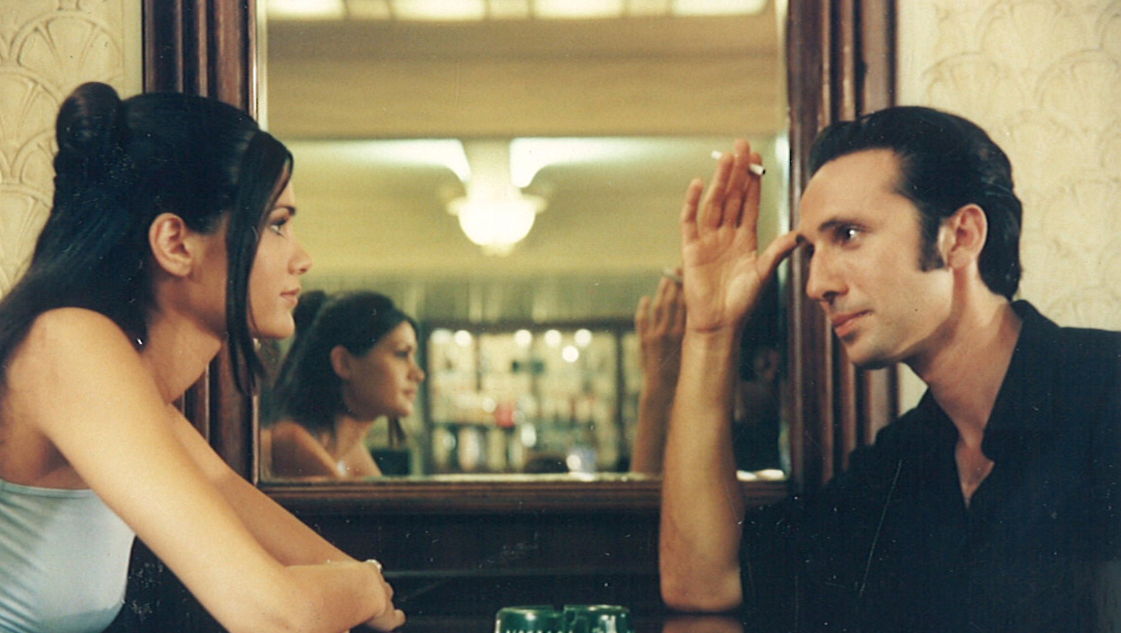 A man and woman sit in a cafe facing each other in front of a mirror