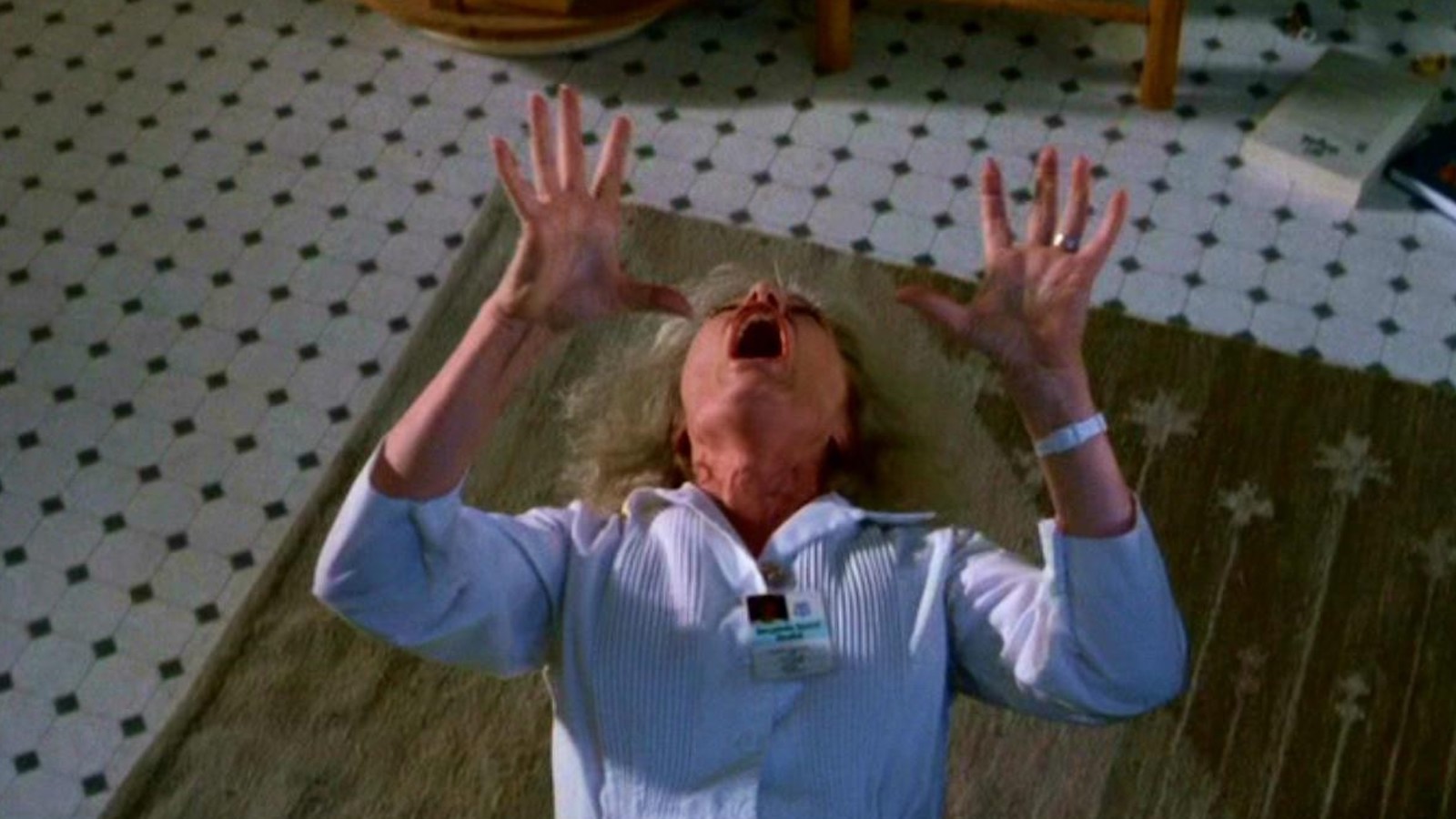 A woman in nurse's uniform falls to floor holding her hands up and screaming