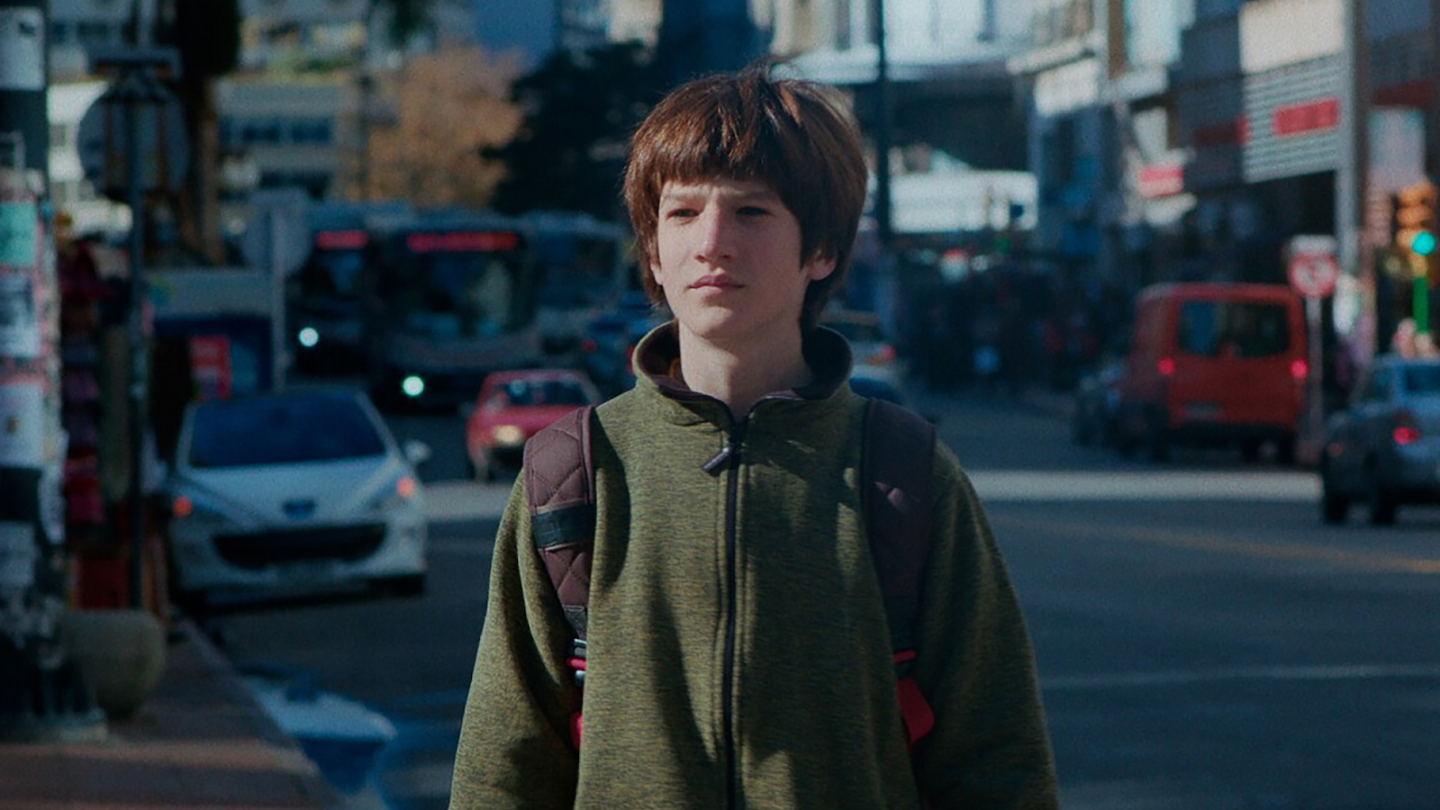 IWokeUpwithaDream2 A boy wearing a sweatshirt and backpack stands in a city street and stares off