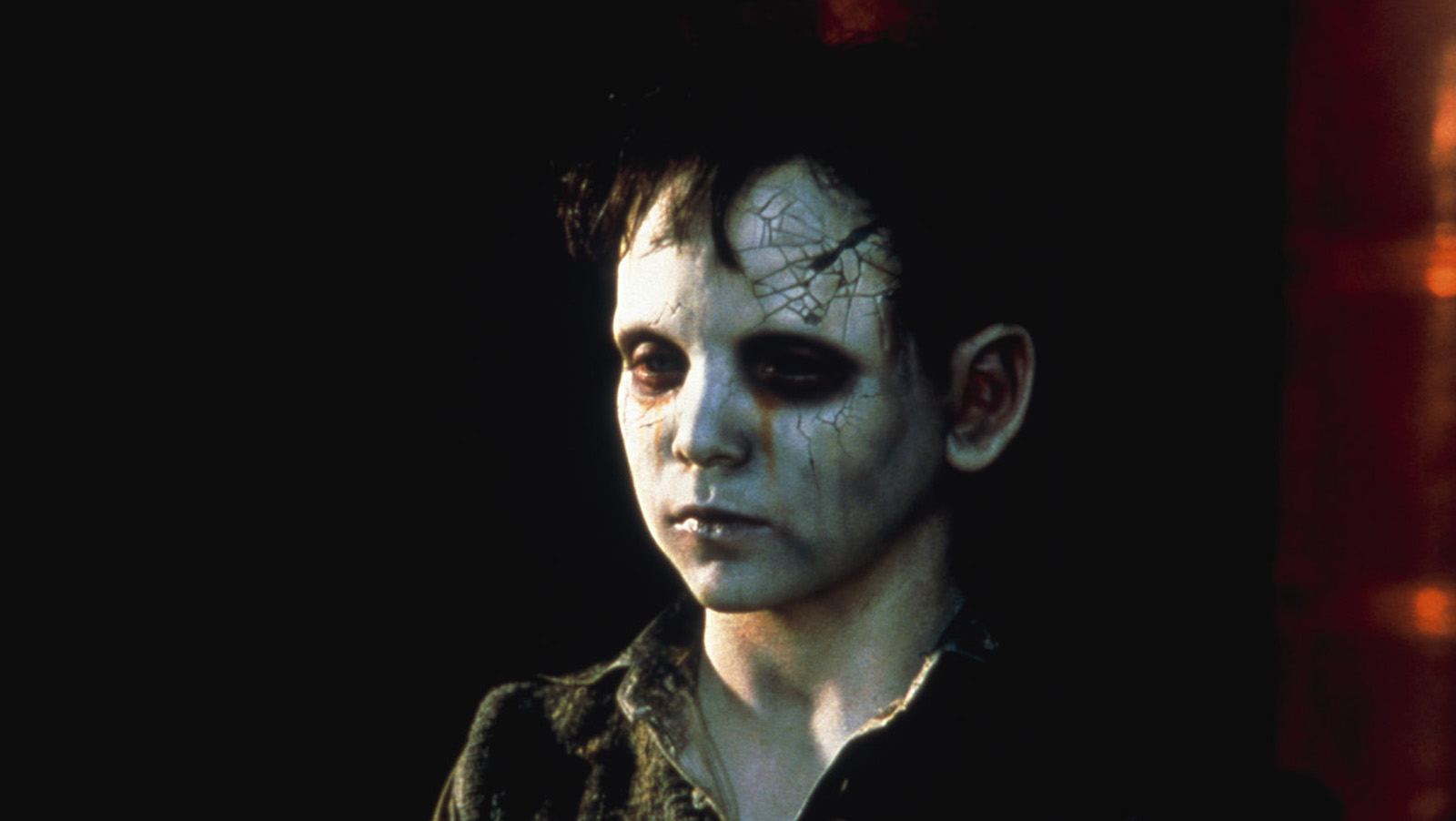 A little zombie boy with a crack in his forehead stares into the distance.