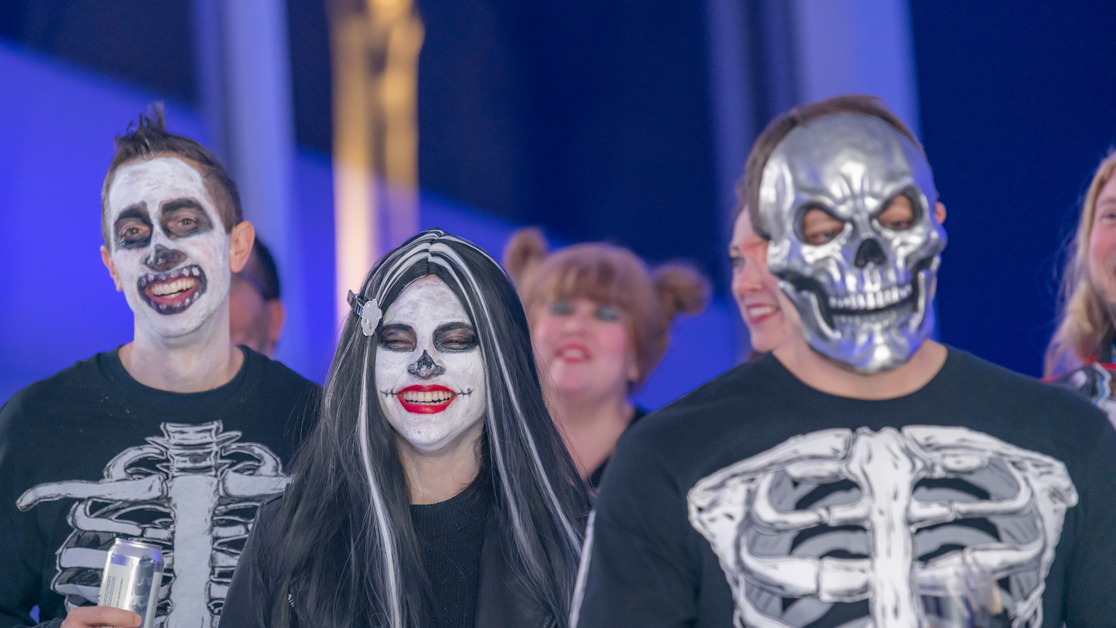 Three Museum goers wearing Halloween costumes and skeleton masks, smiling at the camera during a Halloween party.