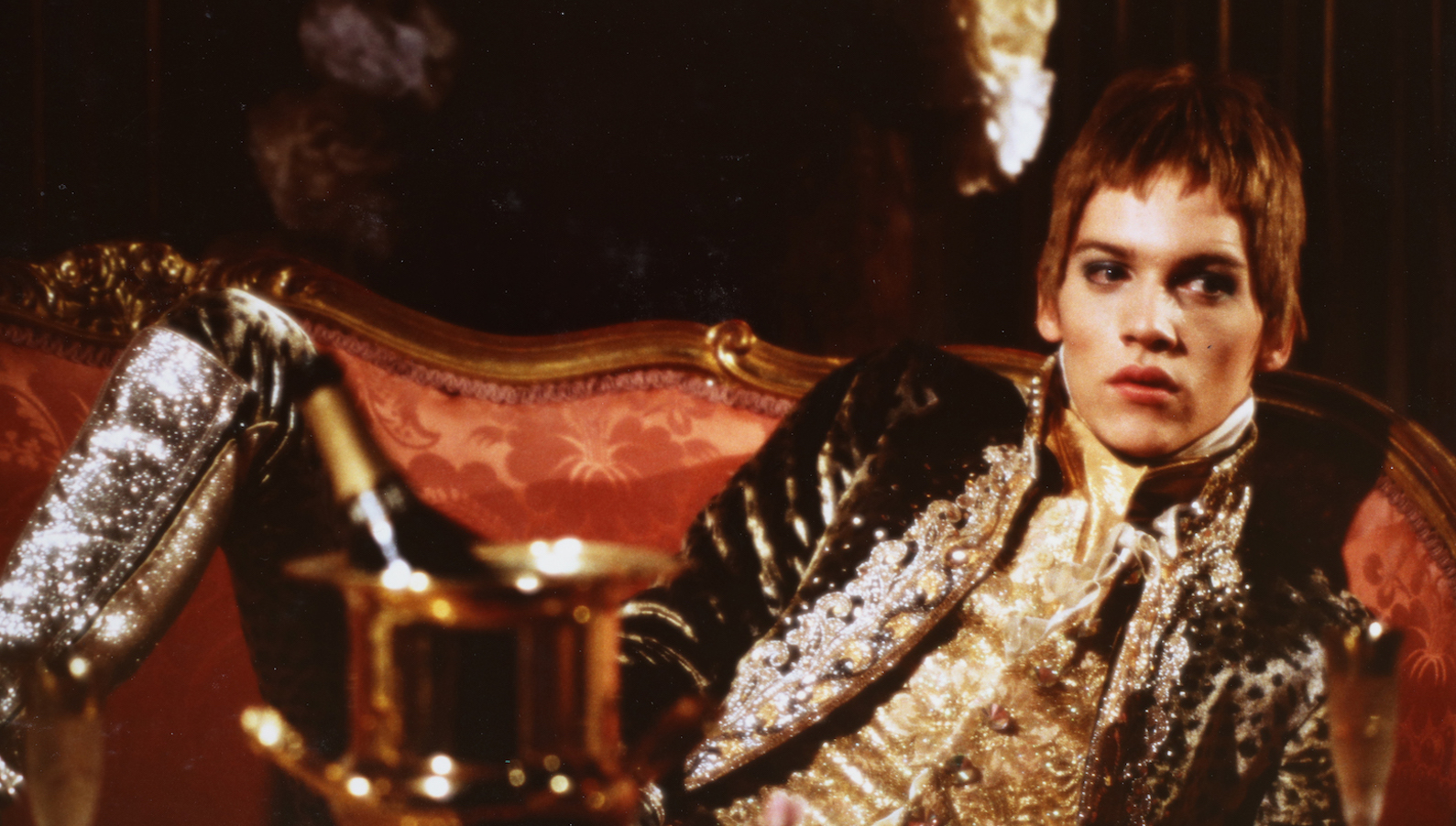A glam rock star in spangled suit reclines on a couch