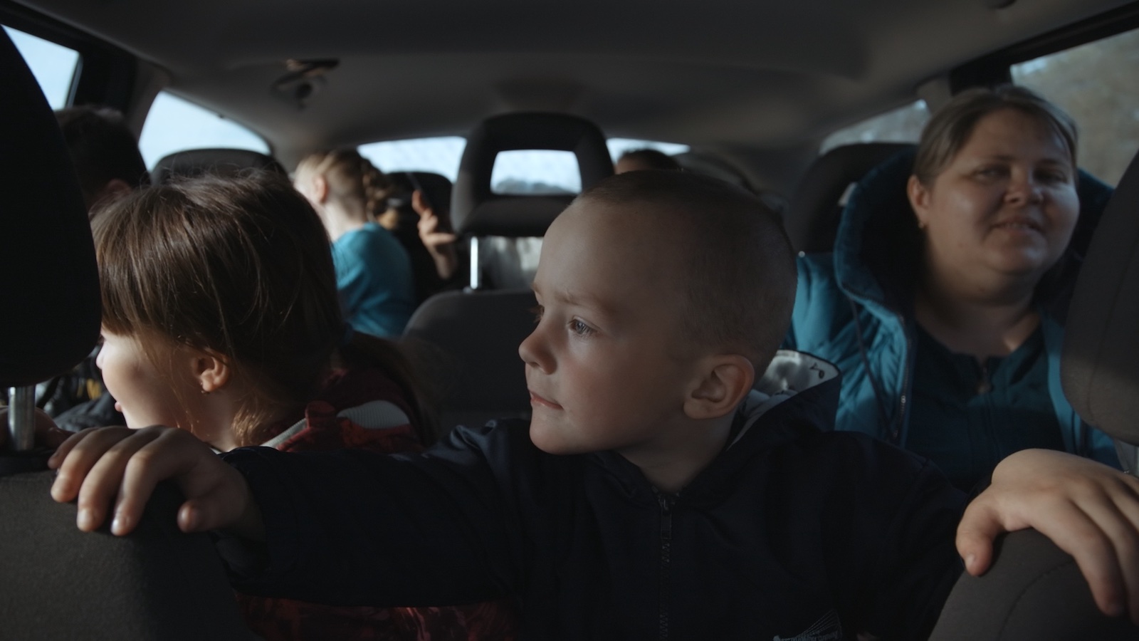 A child sits in the backseat of a car, gripping the headrests of the front seats.