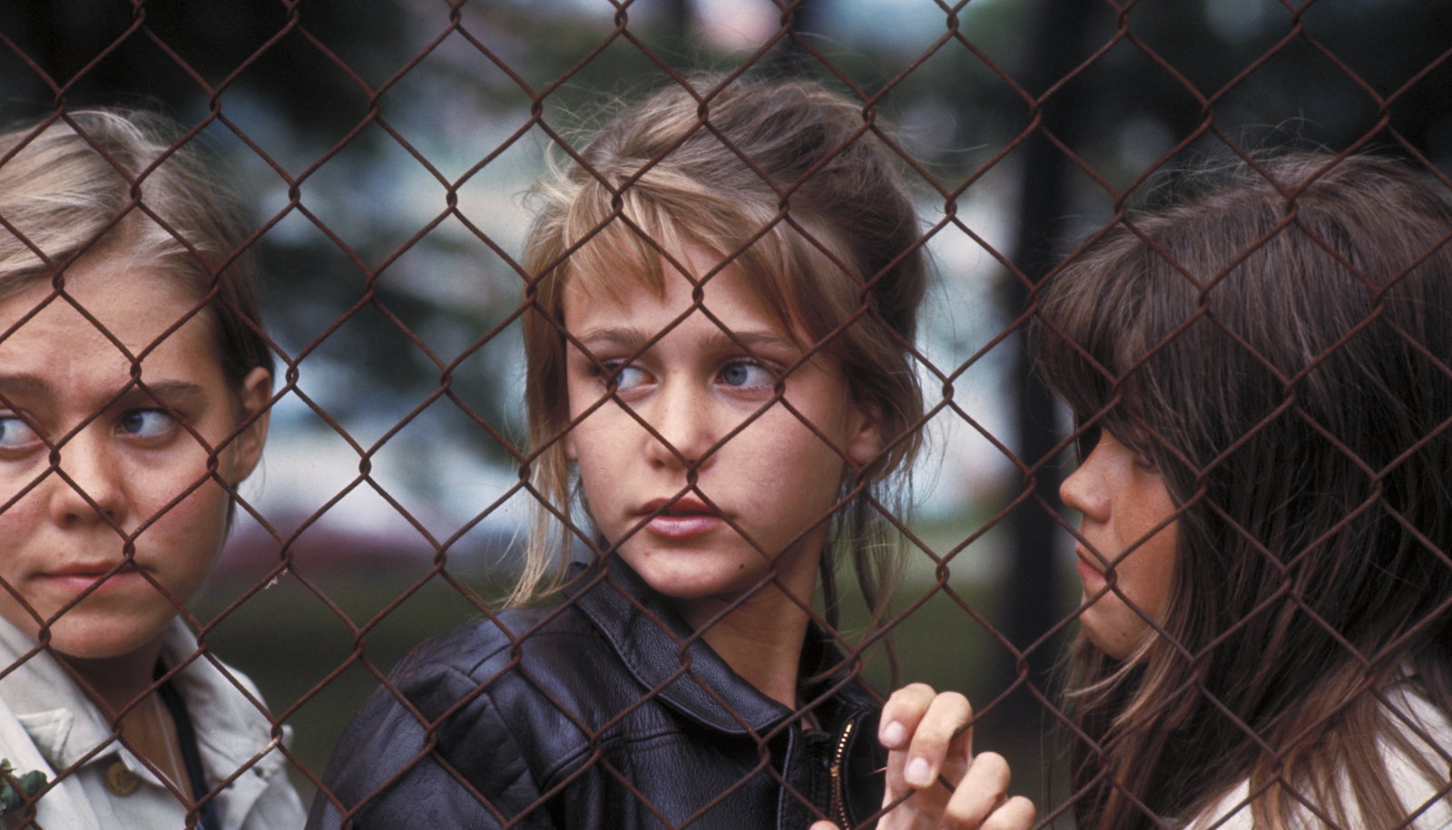 Three girls look through a chain link fence