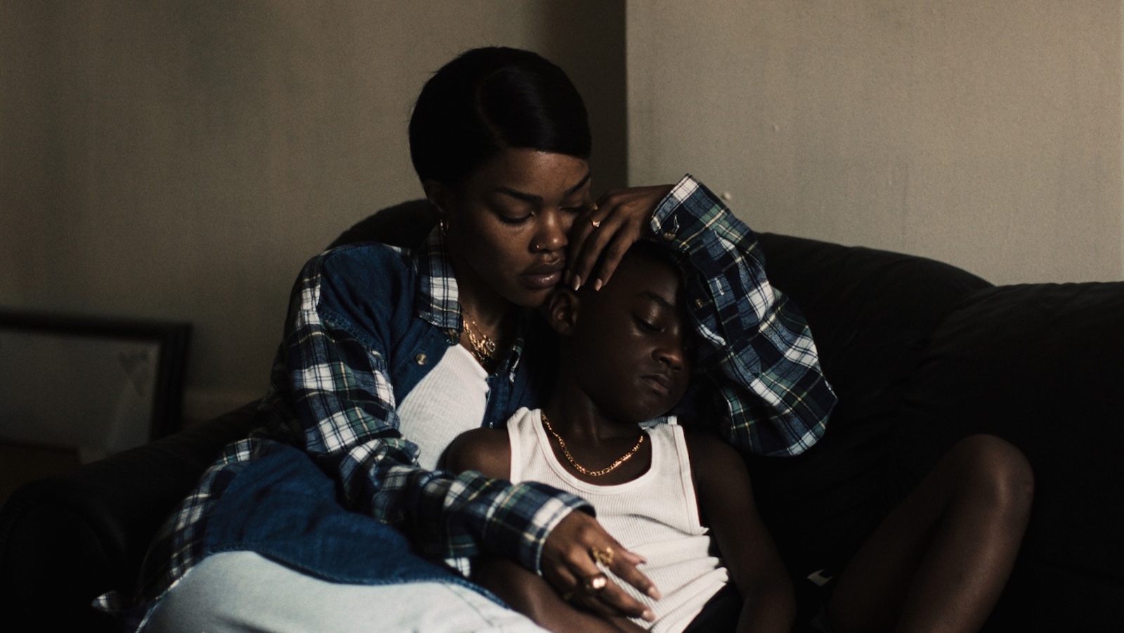 A woman wearing a flannel shirt holds her young son in her arms sitting on a couch