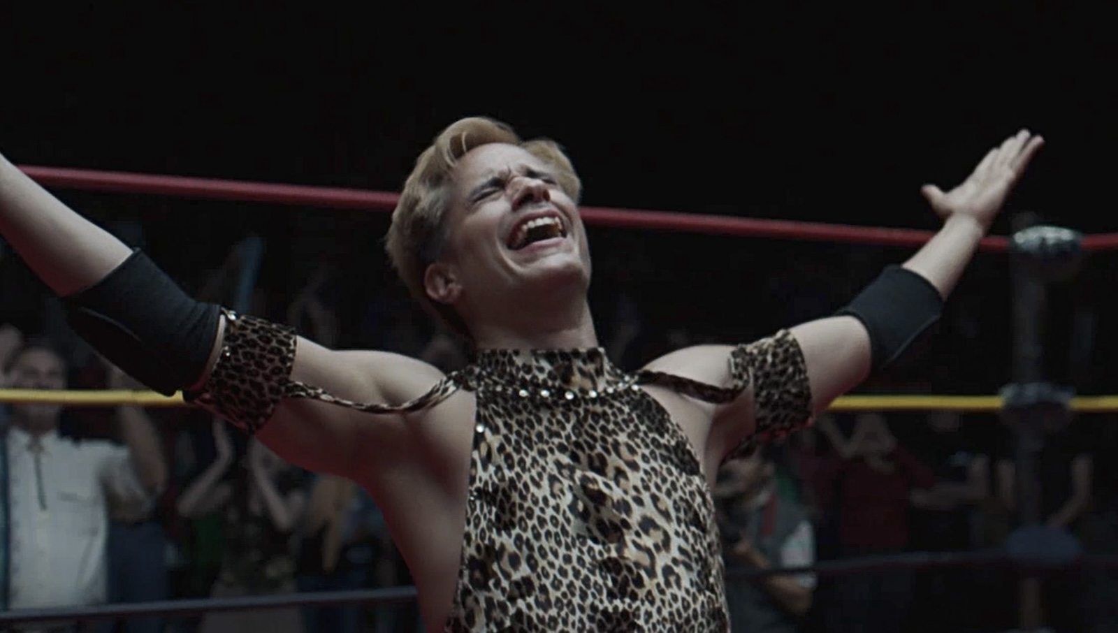 A man in a wrestling outfit on his knees and his arms out