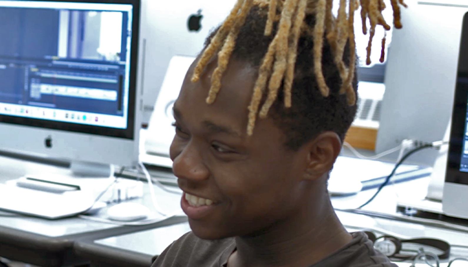 About a Teacher 2 A teenage boy with yellow dreadlocks sits in a classroom surrounded by computers smiling.