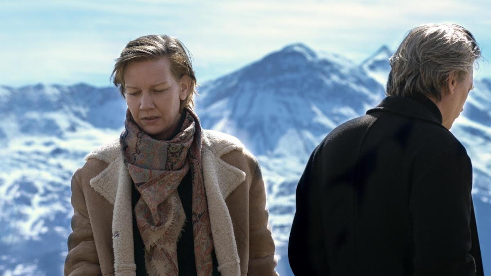Anatomy Of A Fall – Still 3 A man and woman stand with a snowy mountain backdrop, she faces forward hm backward