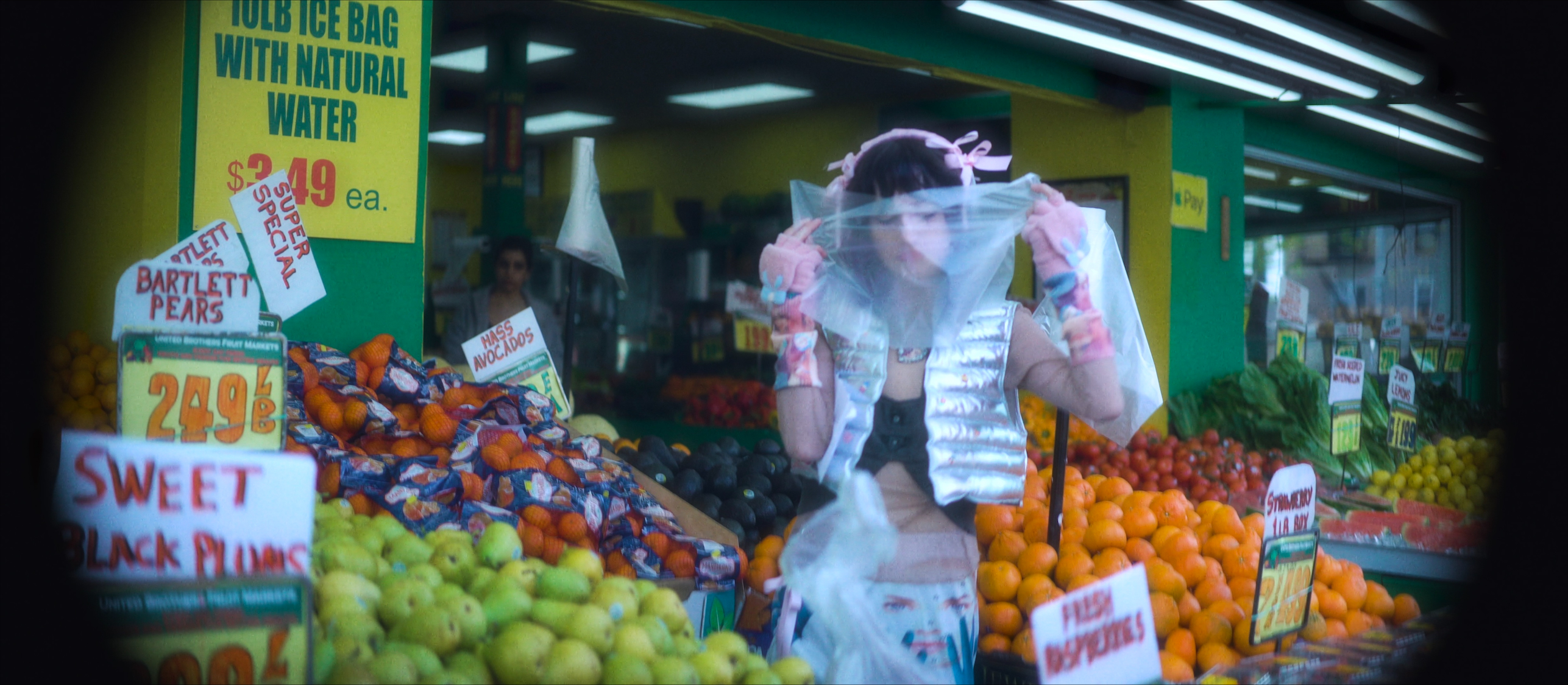 A woman stands in front of an outdoor fruit stand holding a plastic bag over the front of her face