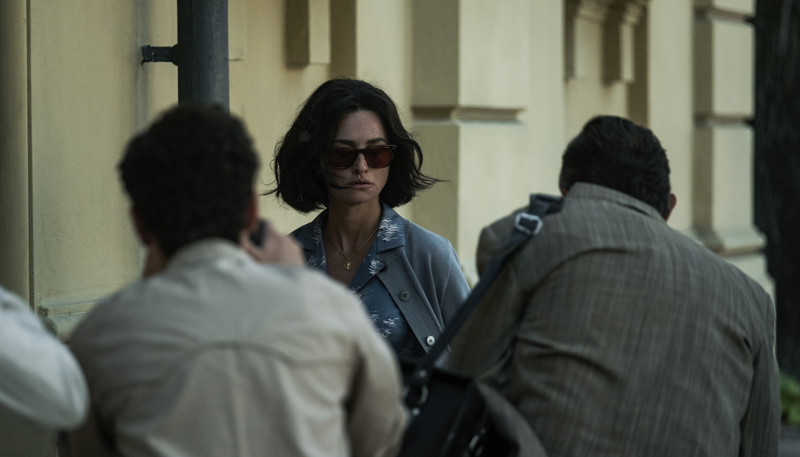 A woman in sunglasses stands on the street, surrounded by photographers