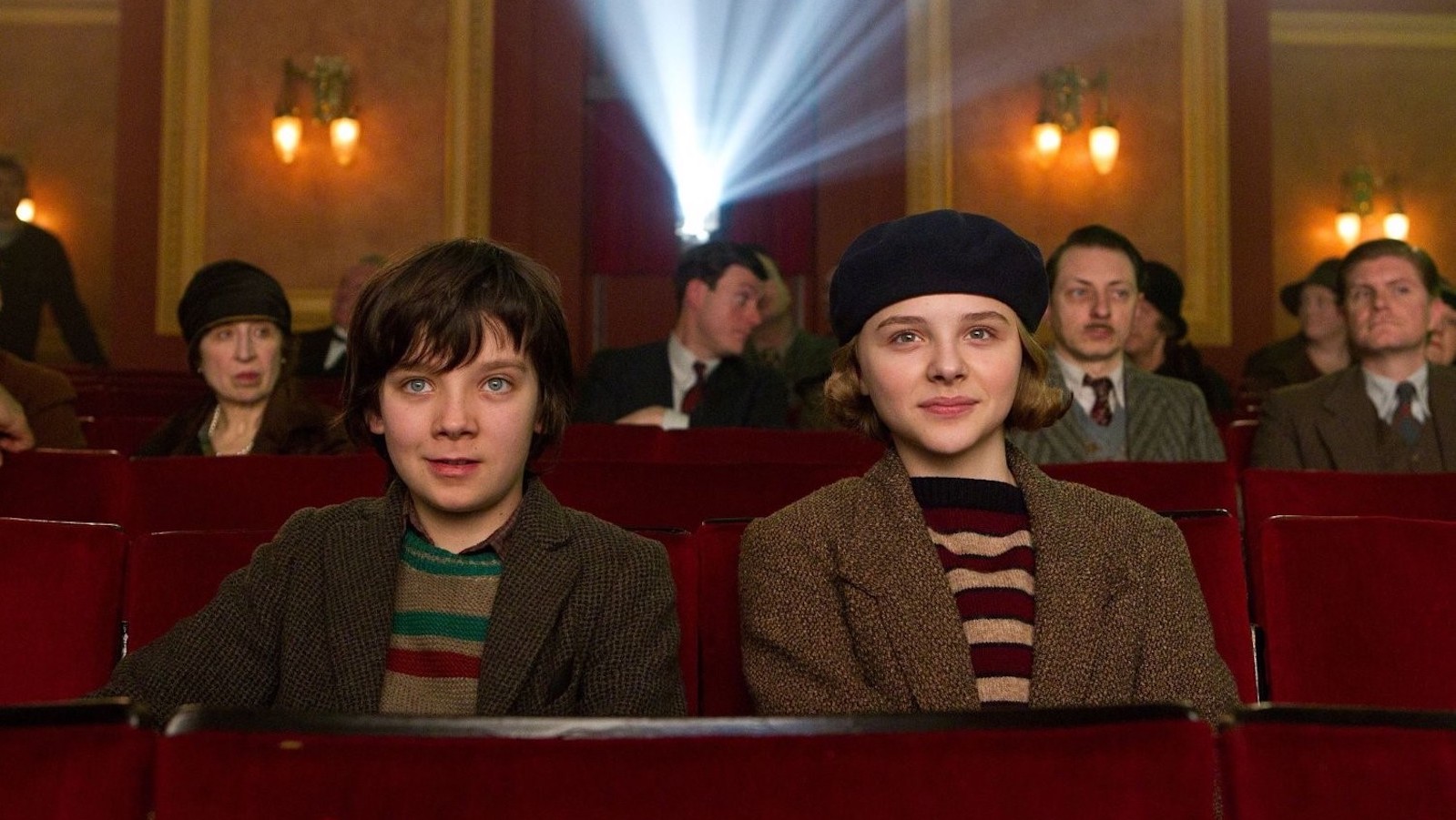Two children look at a screen in a movie theater with the projector light beam behind them.