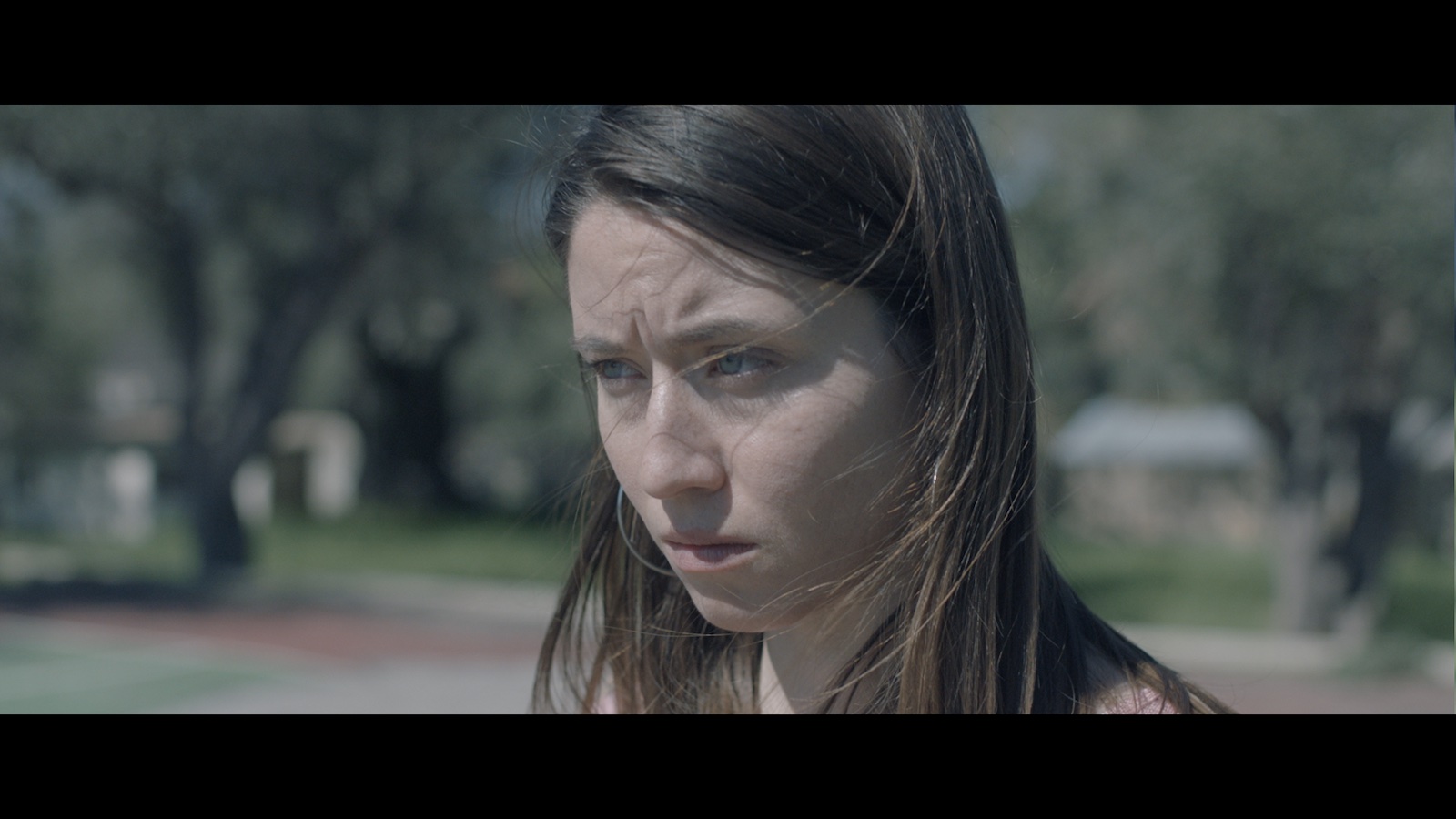 A woman with long stringy hair stands on a street and looks off screen concerned