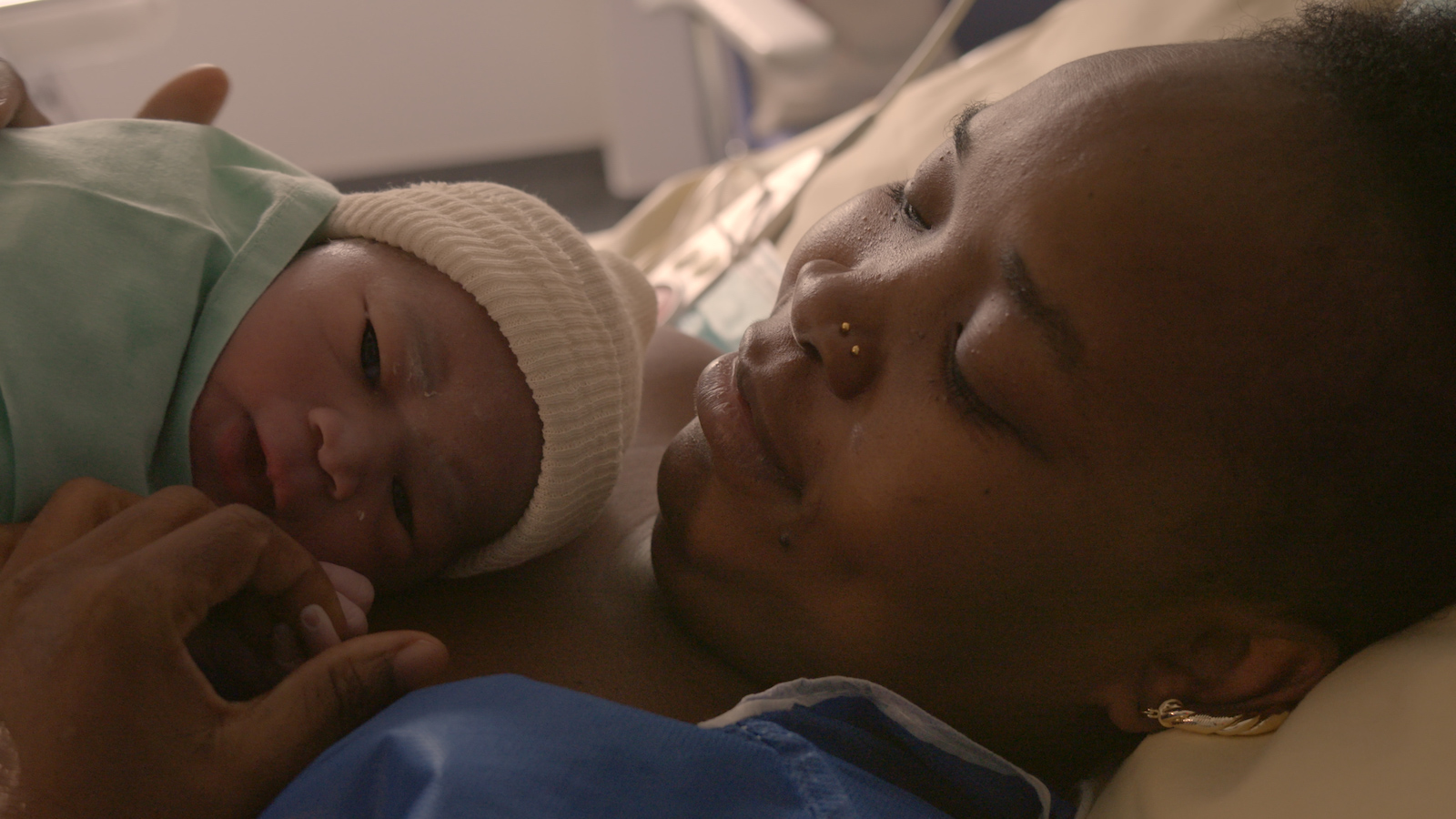 A mother lies with her new baby on her chest, as the woman looks down at her baby and smiles