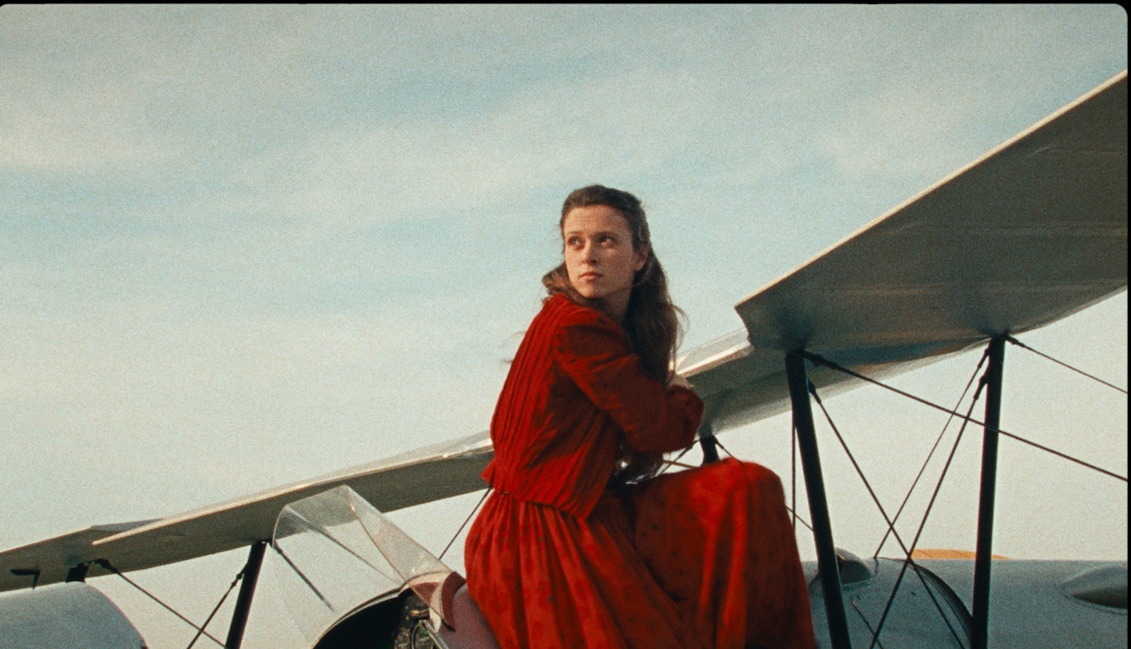 A woman dressed all in red sits on the top of a biplane