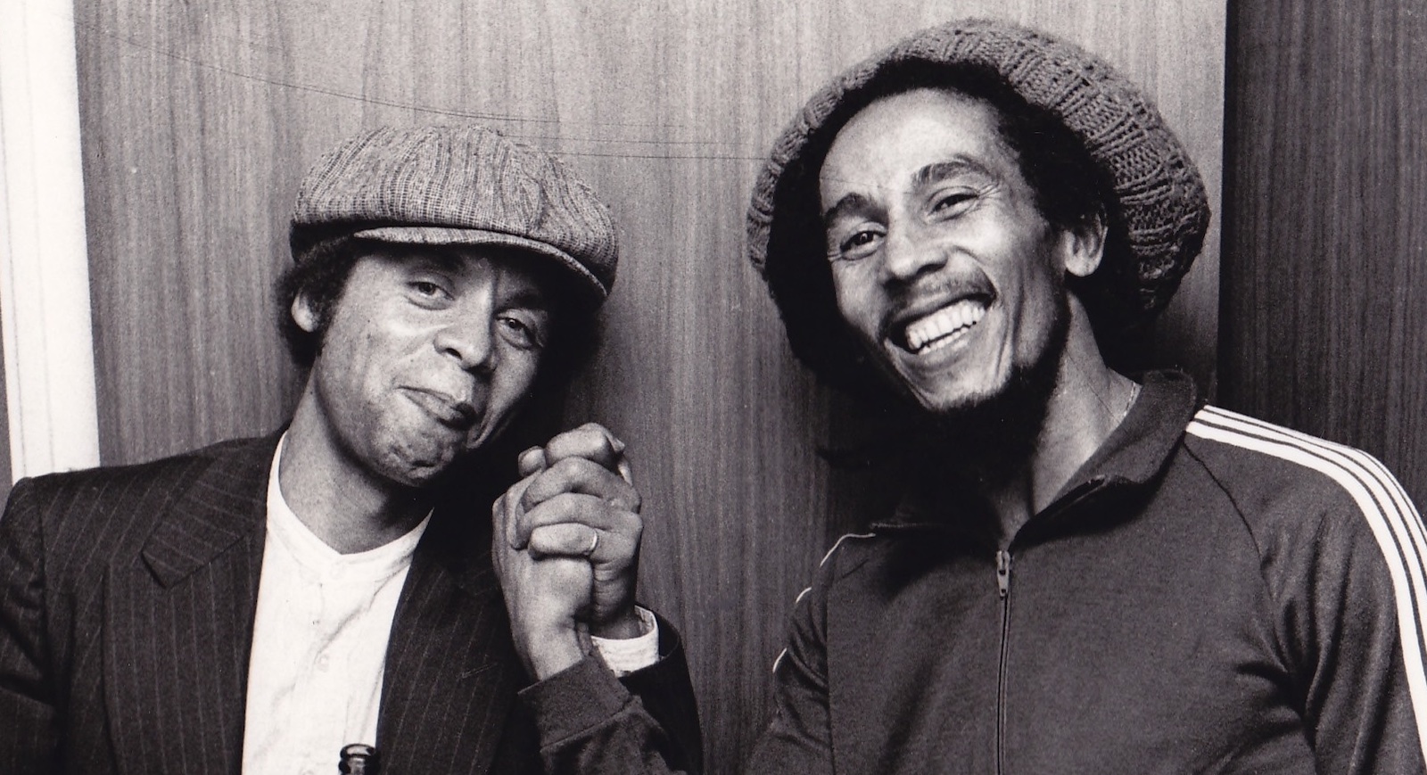 1978 GJ & Bob Marley handshake Two men smile and shake hands against a bare wall in a black-and-white photo