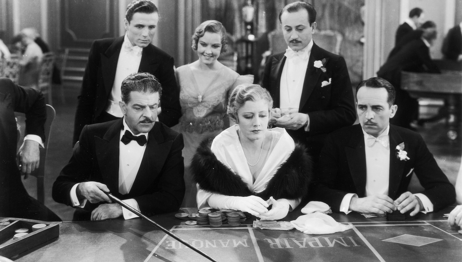 A woman sits at a casino table surrounded by men in a black and white image