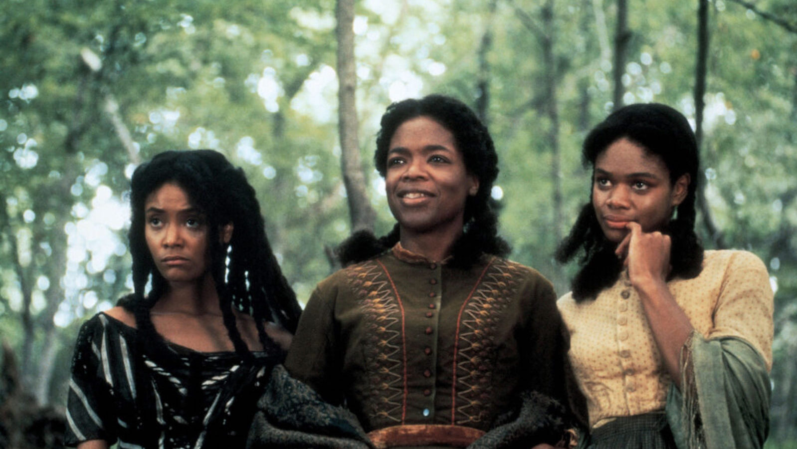 Beloved Three women, one mother and two daughters on either side, stand in a forest looking off past the camera, the mother smiling