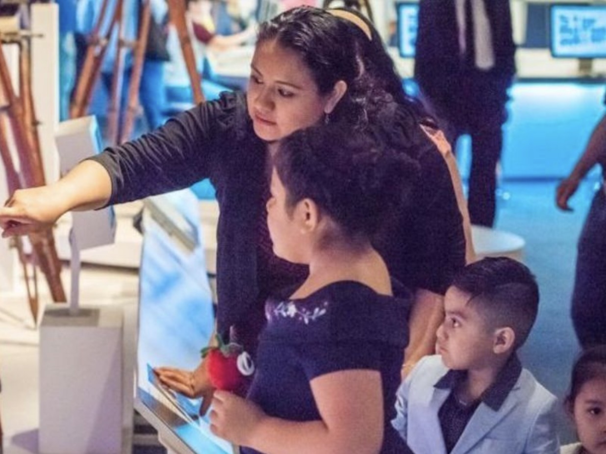 A woman points out cameras in a Museum to two children