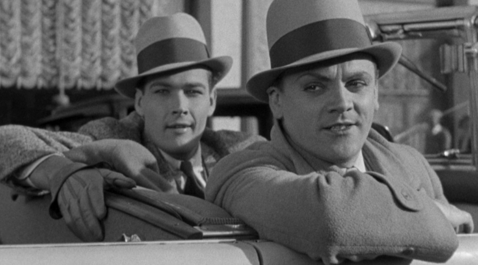 Public Enemy Two gangsters in fedoras sneer from a car in a black and white image