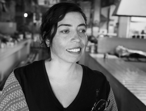 A black and white portrait of a person smiling in medium close-up as she looks off-screen