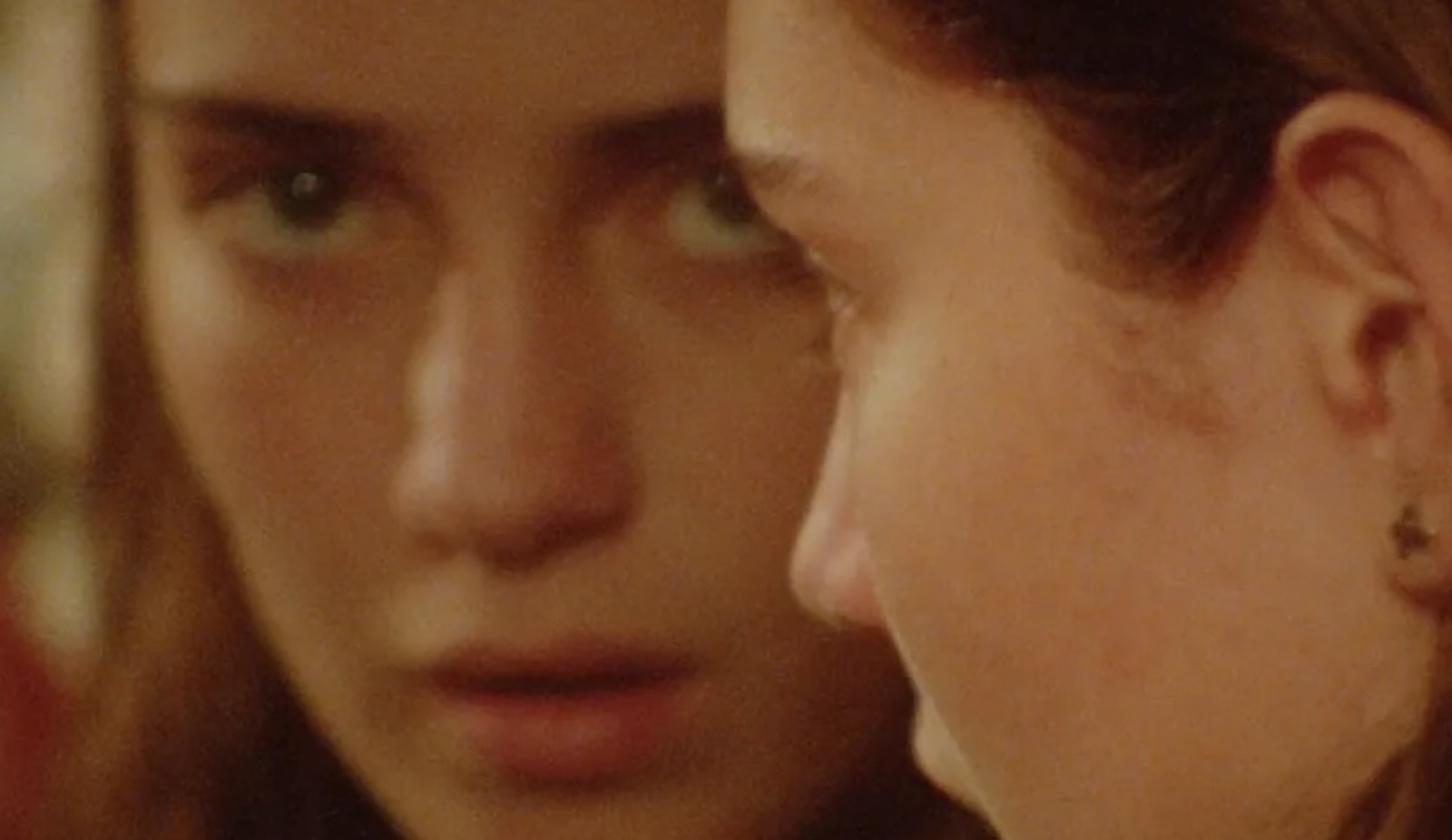 An extreme closeup of a woman looking in a mirror and the camera with a blank expression