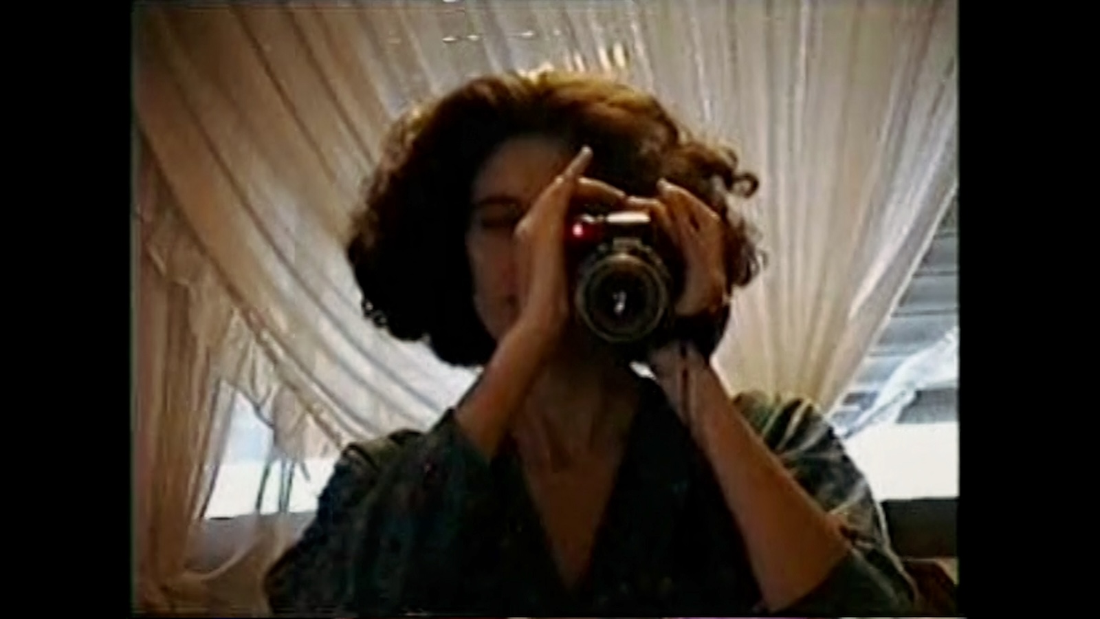 Three Promises An image that looks like slightly degraded video from the eighties or nineties in which a woman holds a camcorder to her eye and aims toward the screen.