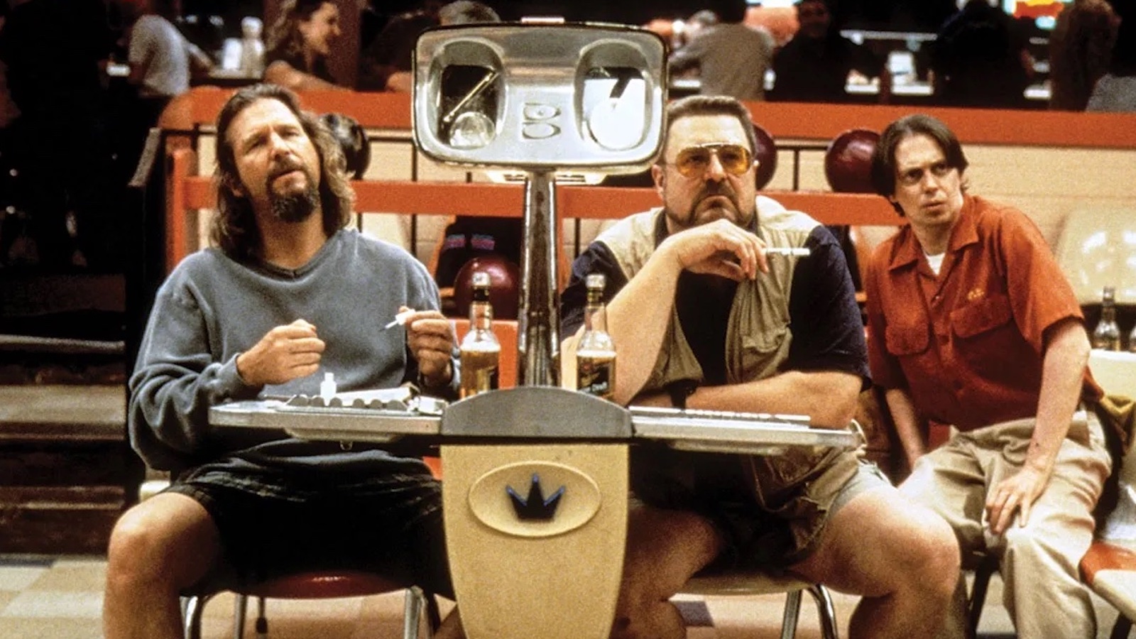 Big Lebowski Three men sit at a bowling alley lane booth, two wearing shorts and one in khakis looking past us quizzically.