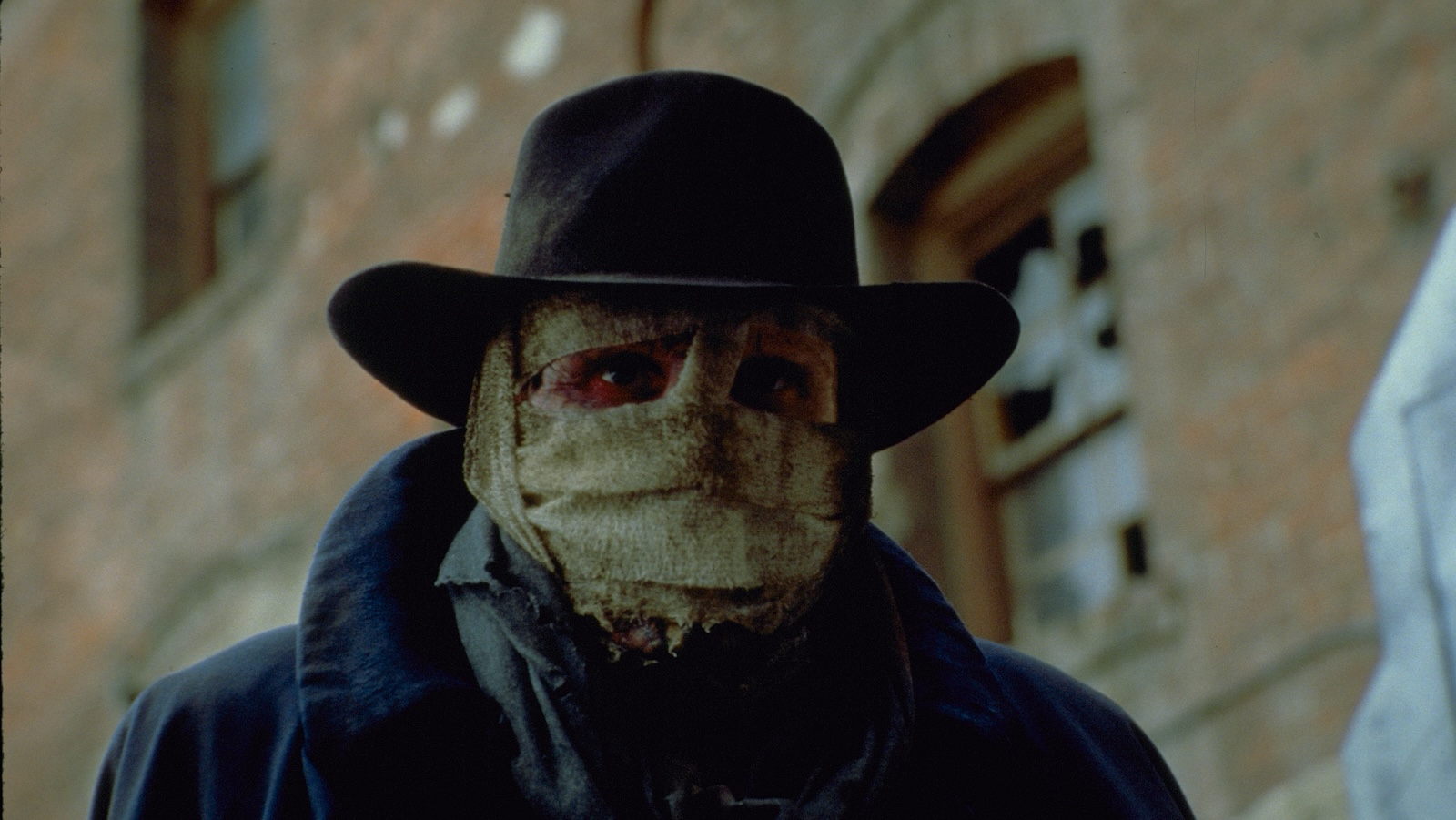 A closeup of a man with a scarred face wrapped in bandages and wearing a black fedora