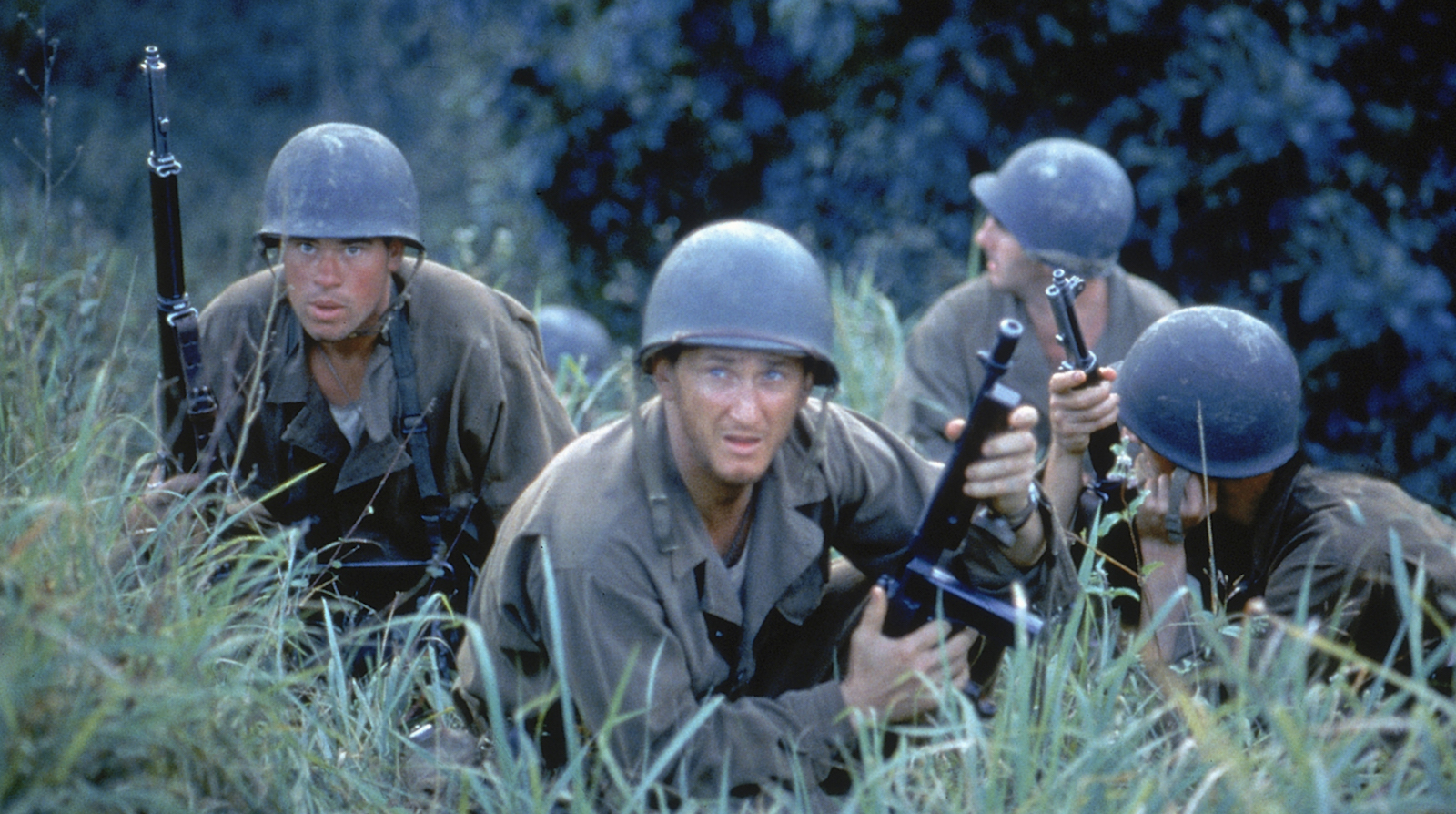 Four soldiers in fatigues and helmet crouch in a field of tall grass