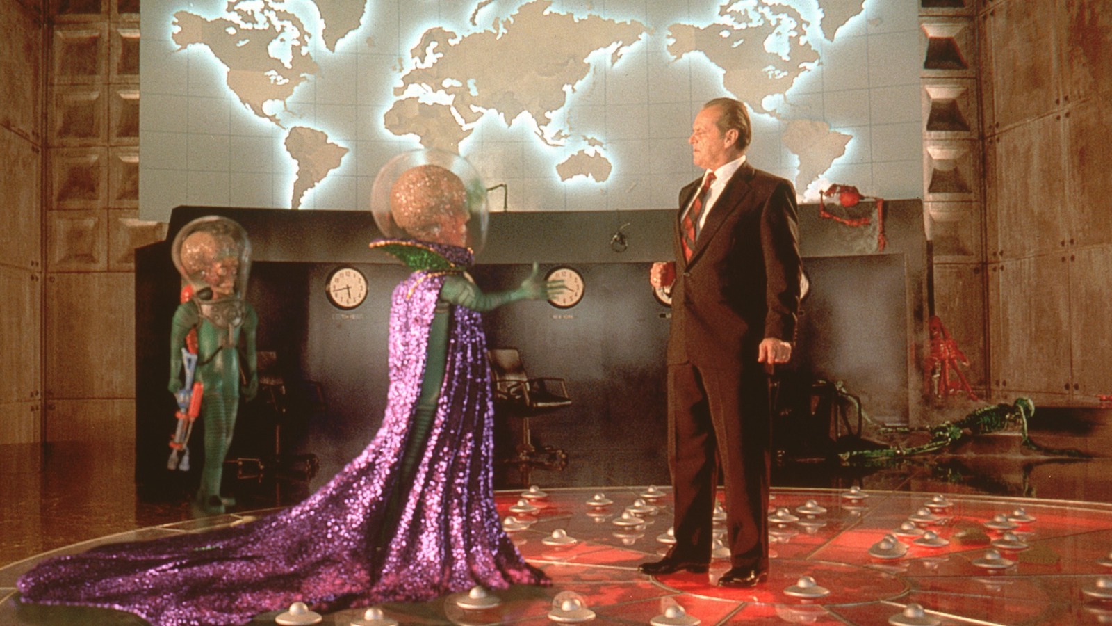 A silly-looking skeleton-faced martian with a huge brain reaches out its hand to shake the hand of a hesitant human man in a brown suit with a map of the world behind them