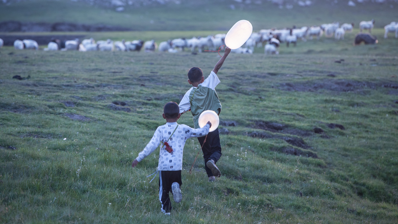 Two children running with balloons in a field
