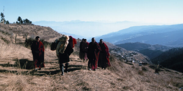 A group of Tibetan monks in red robes walk up a mountainside against a blue sky.