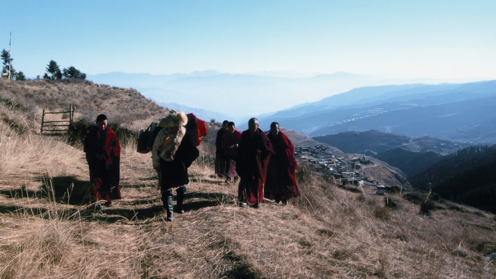 A group of Tibetan monks in red robes walk up a mountainside against a blue sky.