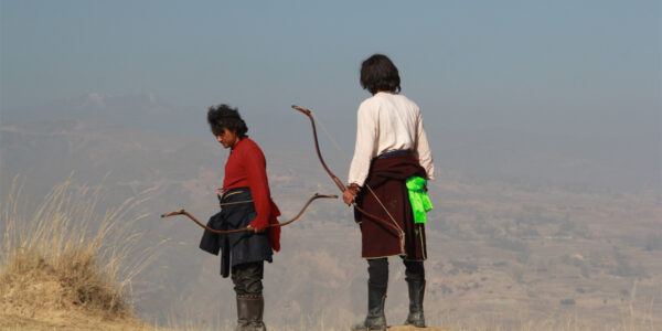 Two archers, holding bows, one in red, one in white, stand against a vast mountainous backdrop