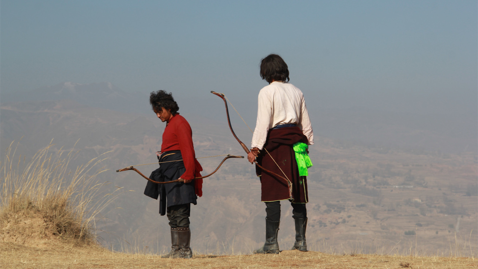 Two archers, holding bows, one in red, one in white, stand against a vast mountainous backdrop