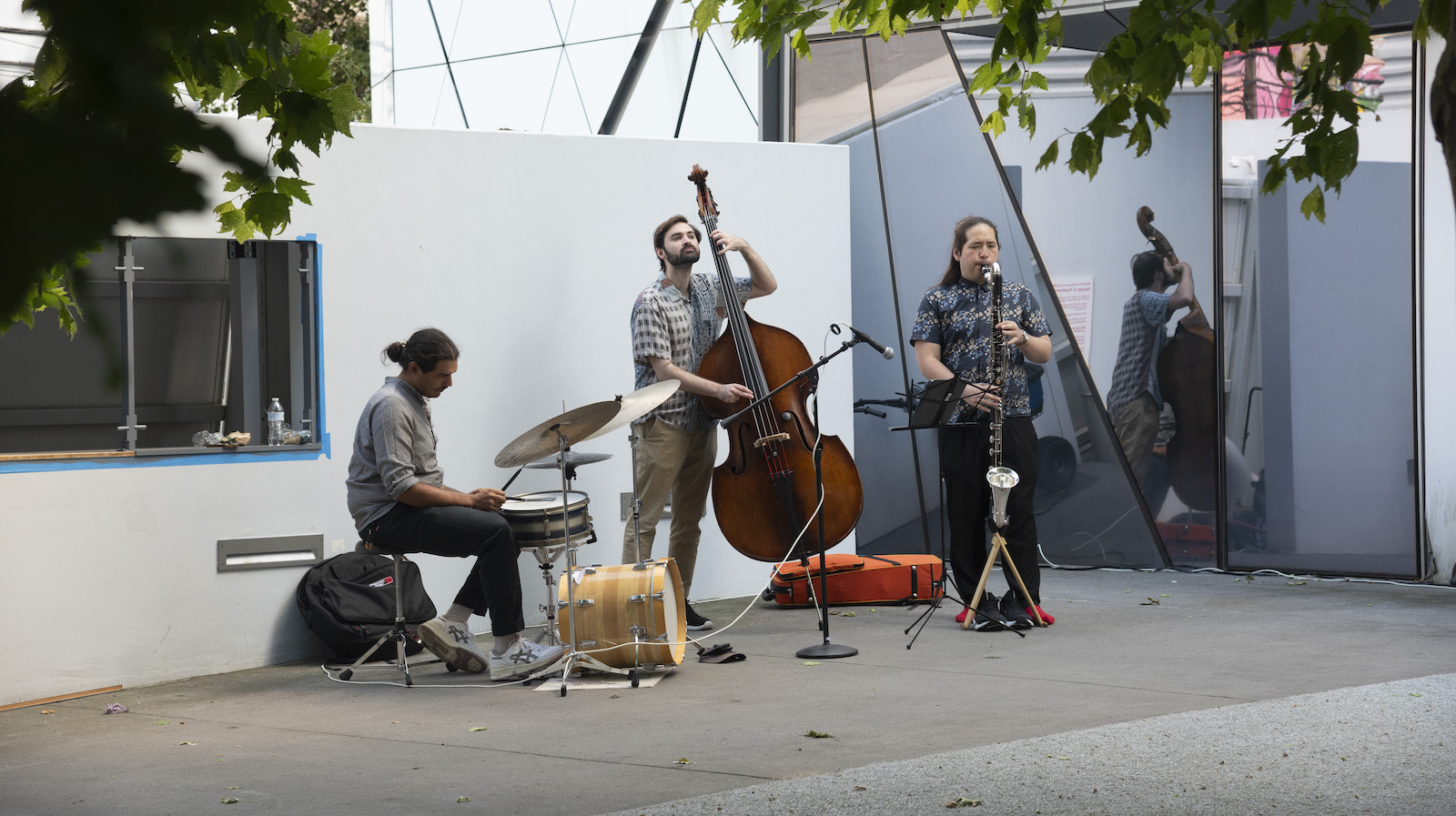 Three musicians—from left, on drums, bass, and clarinet—perform in a courtyard.