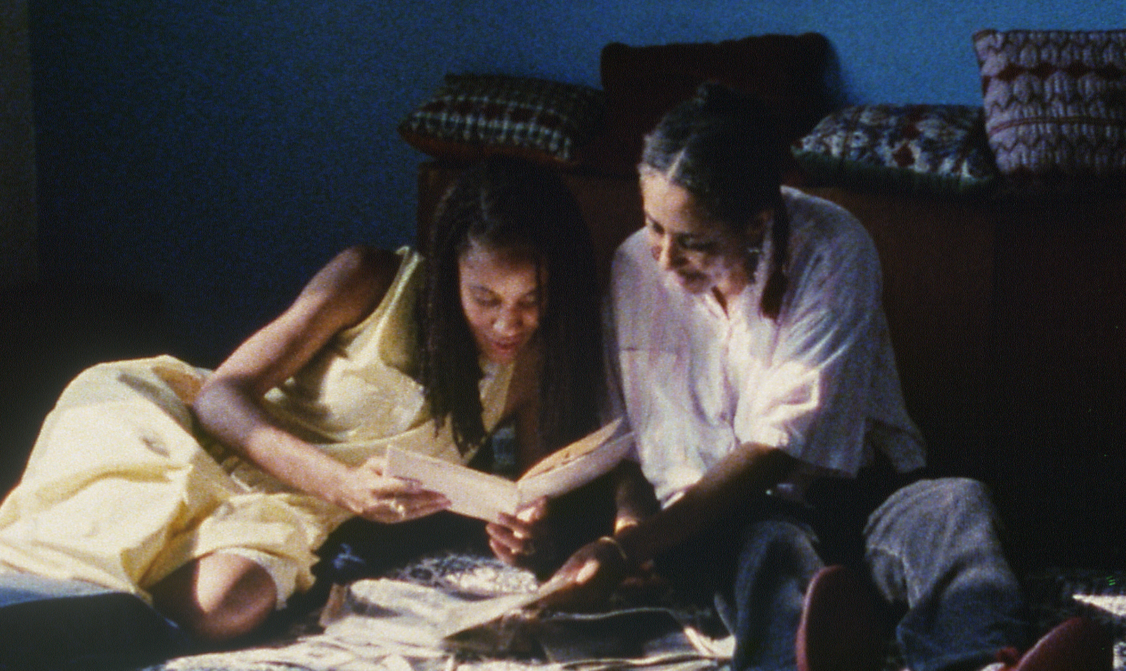 Two women sit on a bed together reading a greeting card