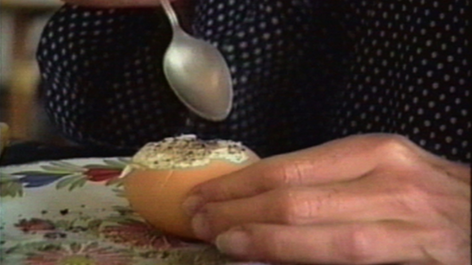 Les Oeufs A spoon hovers over a hard boiled egg, with part of the shell still on.