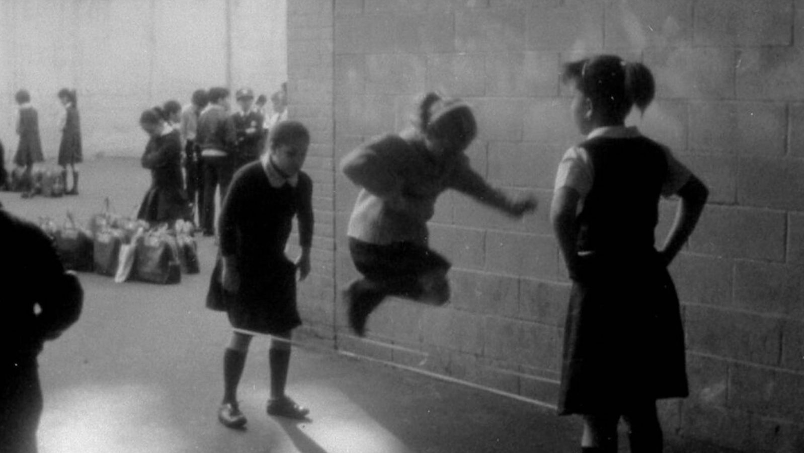 Three girls in school uniforms skip rope in a schoolyard