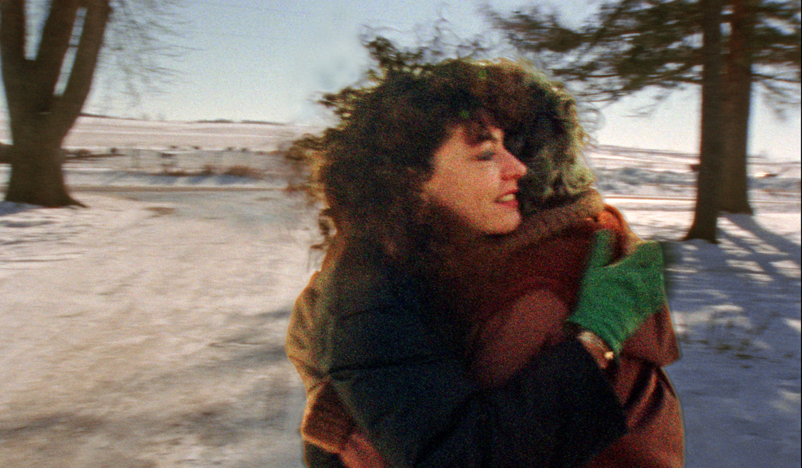 Two women hug each other outside against a snowy landscape with bare trees