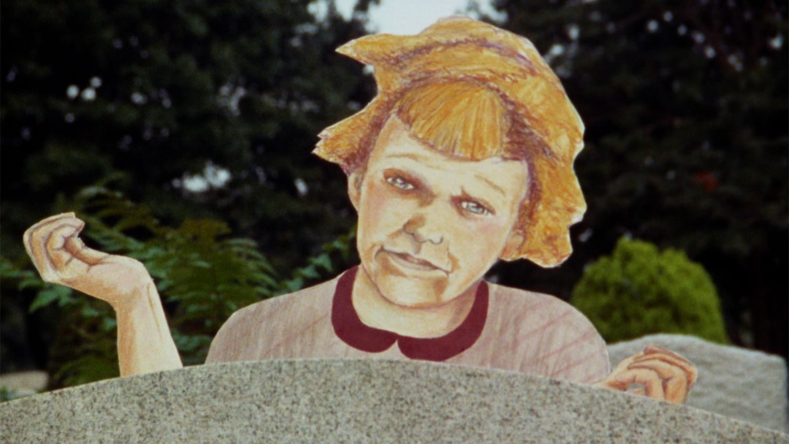 A cardboard cutout of a red-headed child puts its hands in the air, perched in front of a tree.
