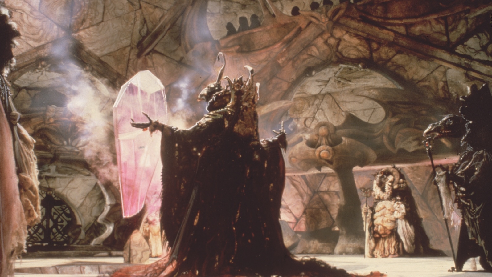 A fantastical creature opens its arms to a large pink floating crystal, surrounded by other creatures holding staffs