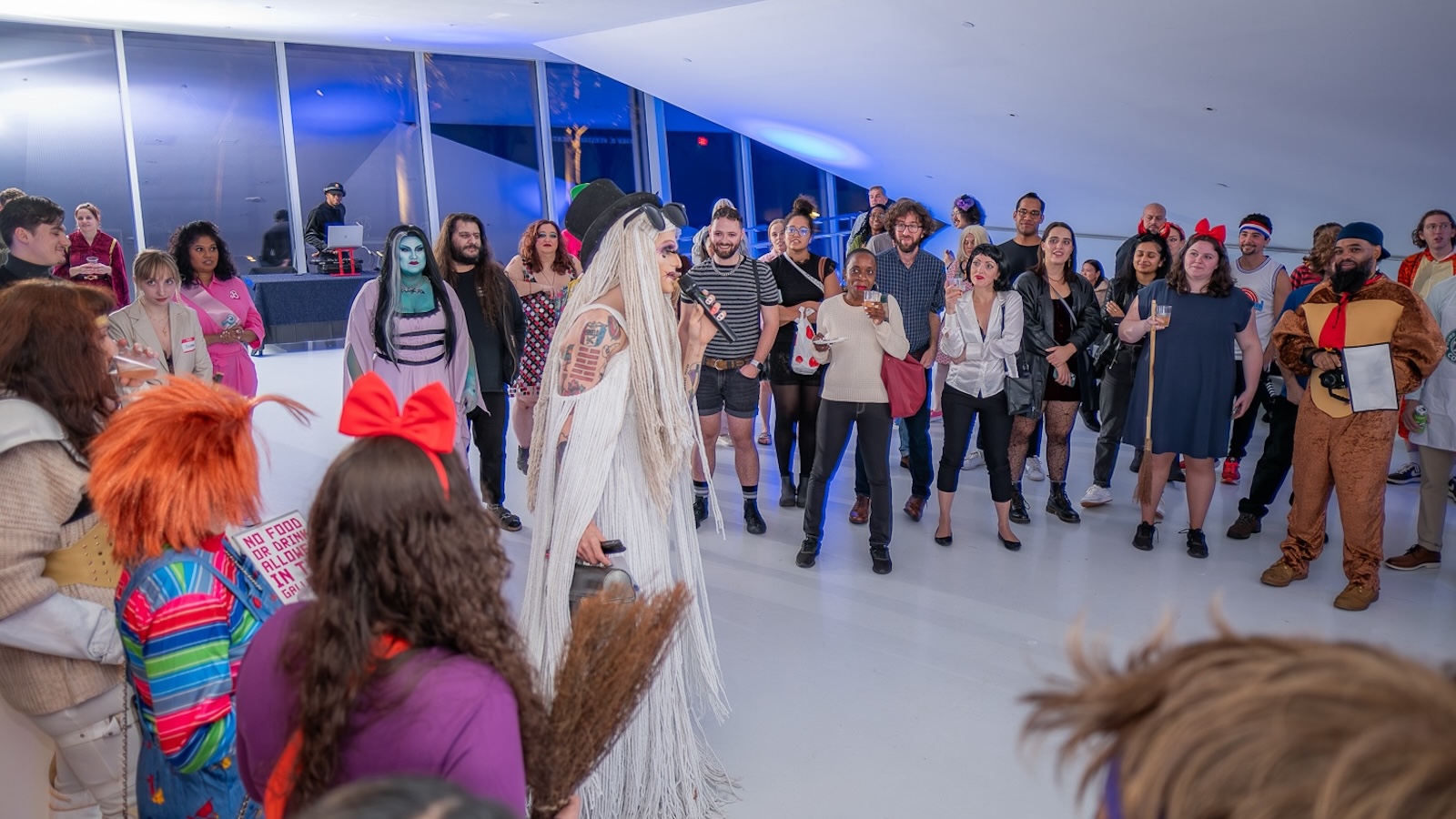 A group of people in Halloween costumes stand merrily in the Museum of the Moving Image lobby in the evening.