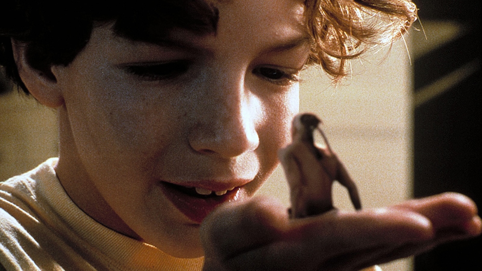 A little boy holds a tiny, toy-sized man wearing a Native American headdress in his hand