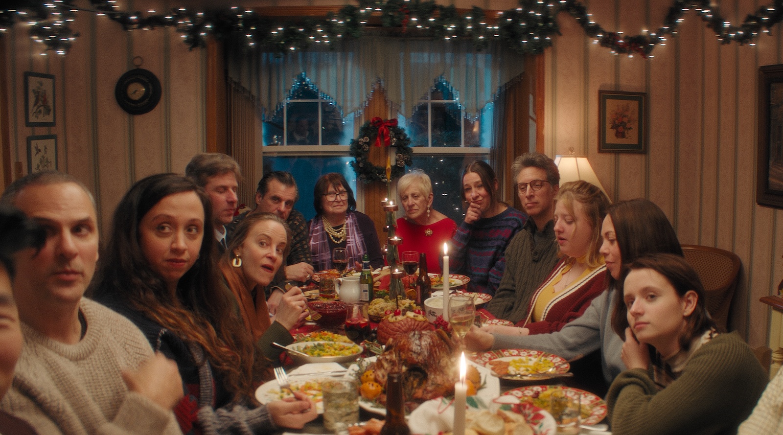 A group of people sit around a dinner table at Christmas surrounded by lights and a wreath