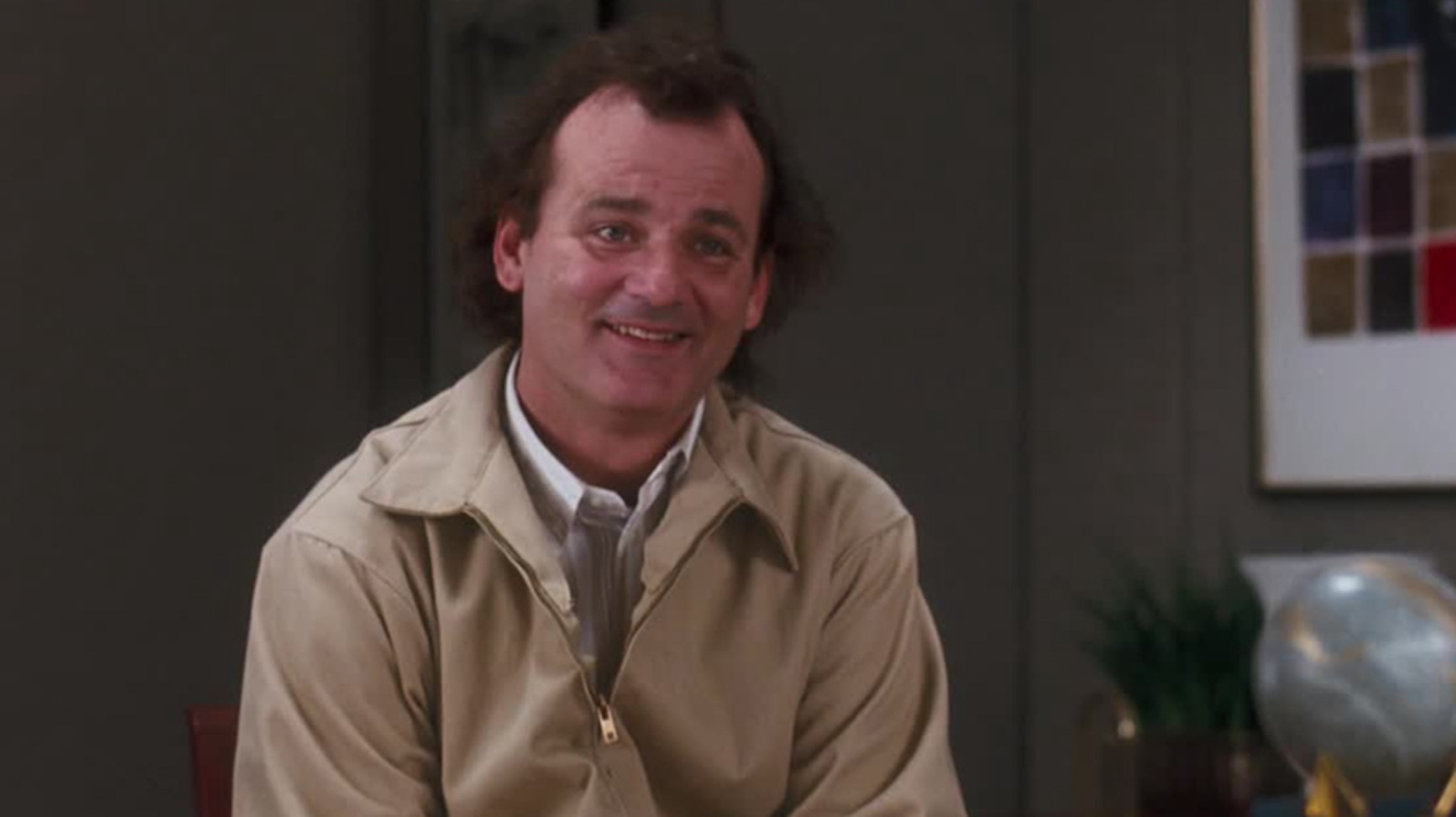 A man smiles into the camera, wearing a beige members only jacket