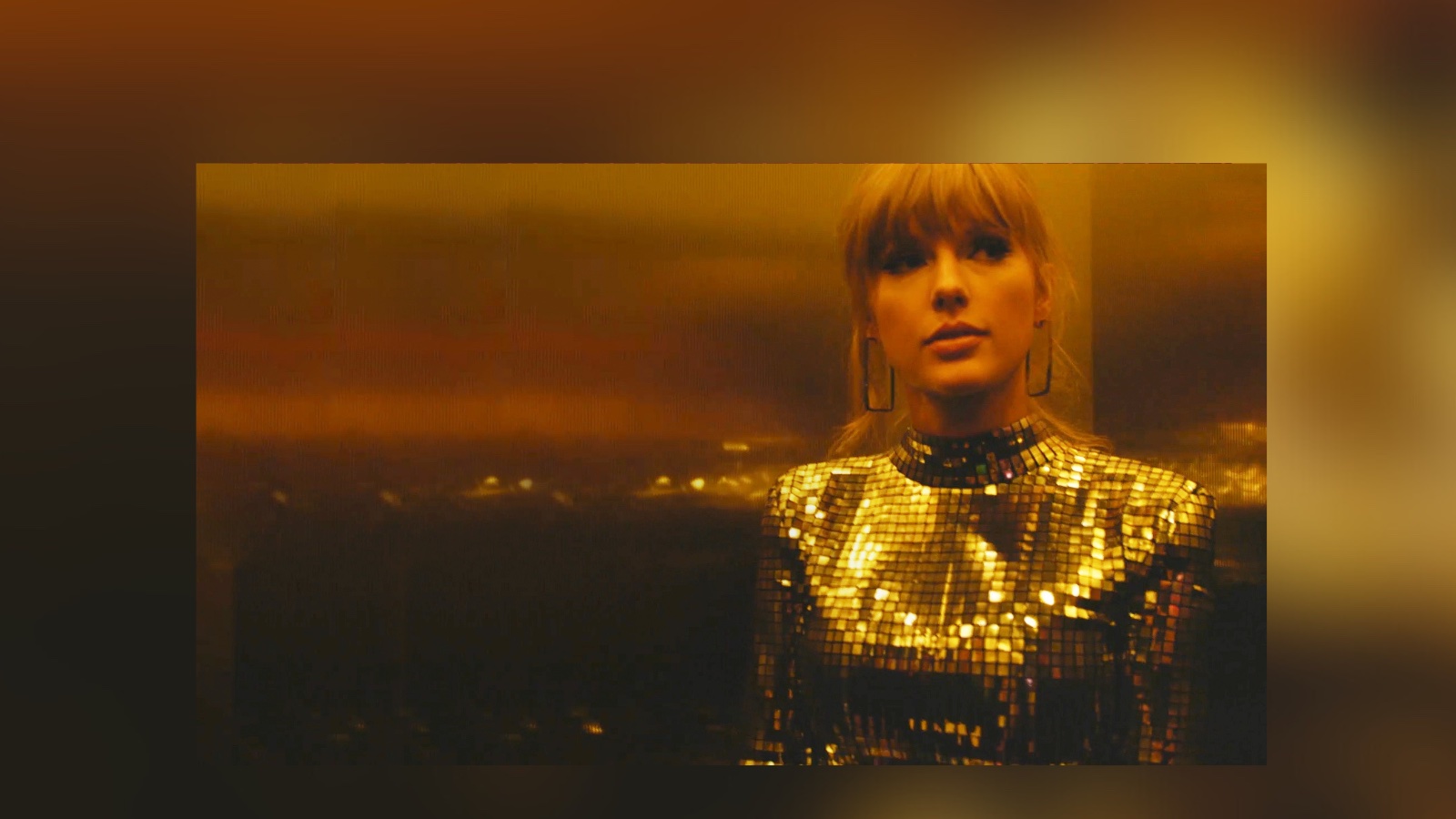 A blonde woman in a glittering silver dress stands against a window showing a vast city backdrop and yellow sky. The woman is Taylor Swift.