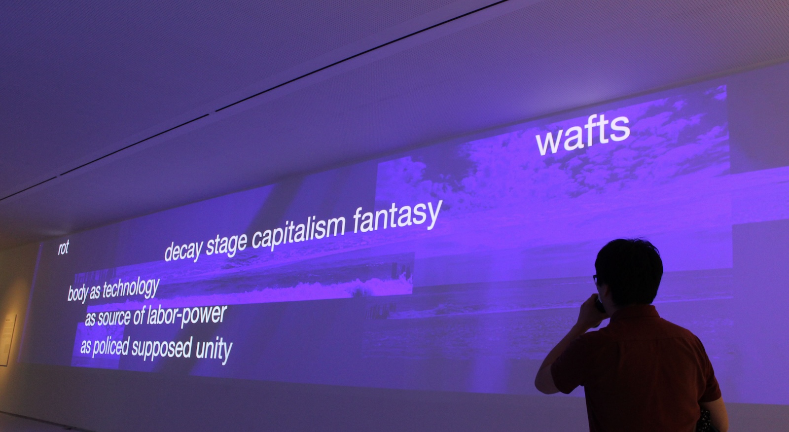 A purple screen at a Museum showing an installation with text scrolling across it with a silhouetted figure looking up at it.