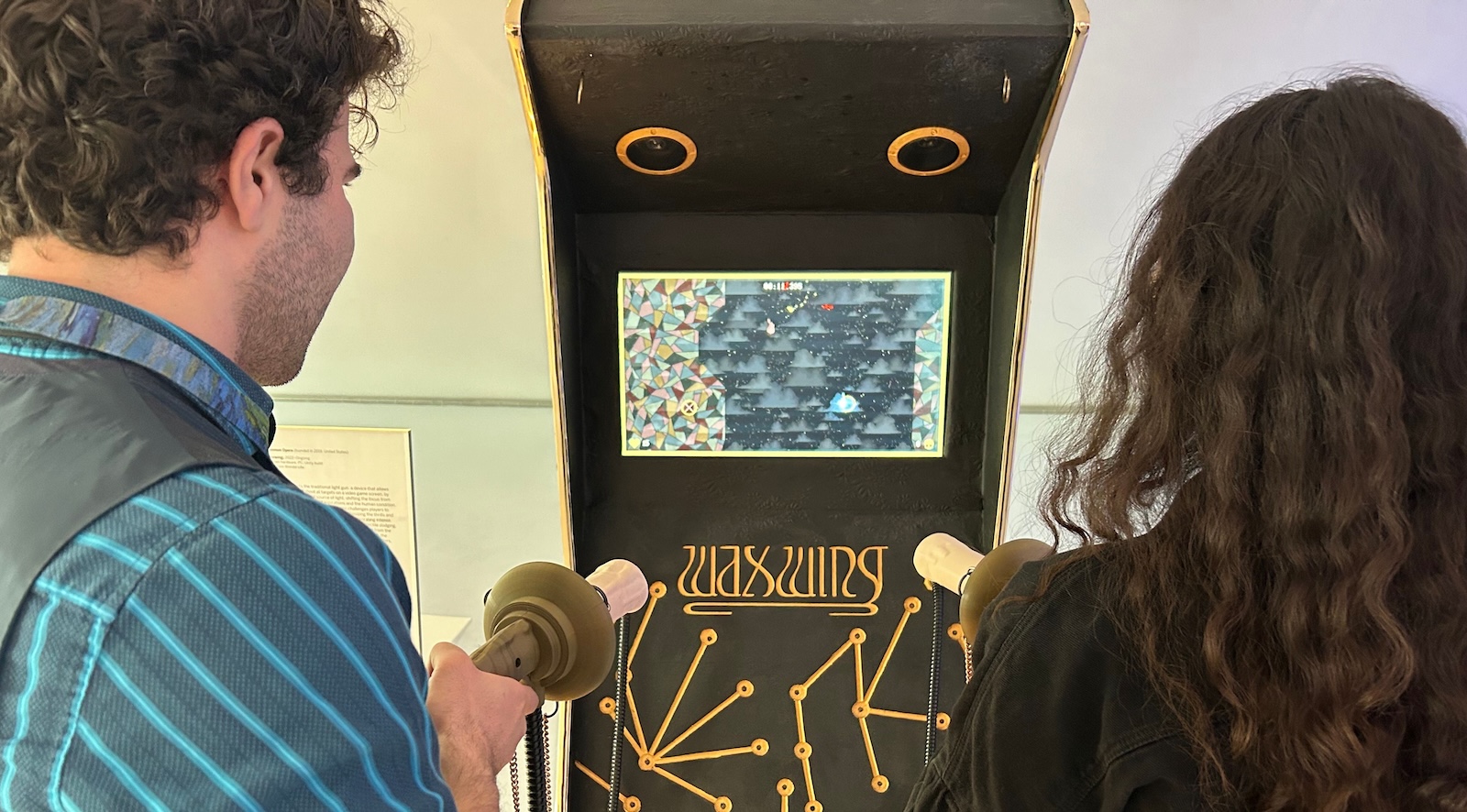 Two people seen from behind aim light guns at an arcade video game screen