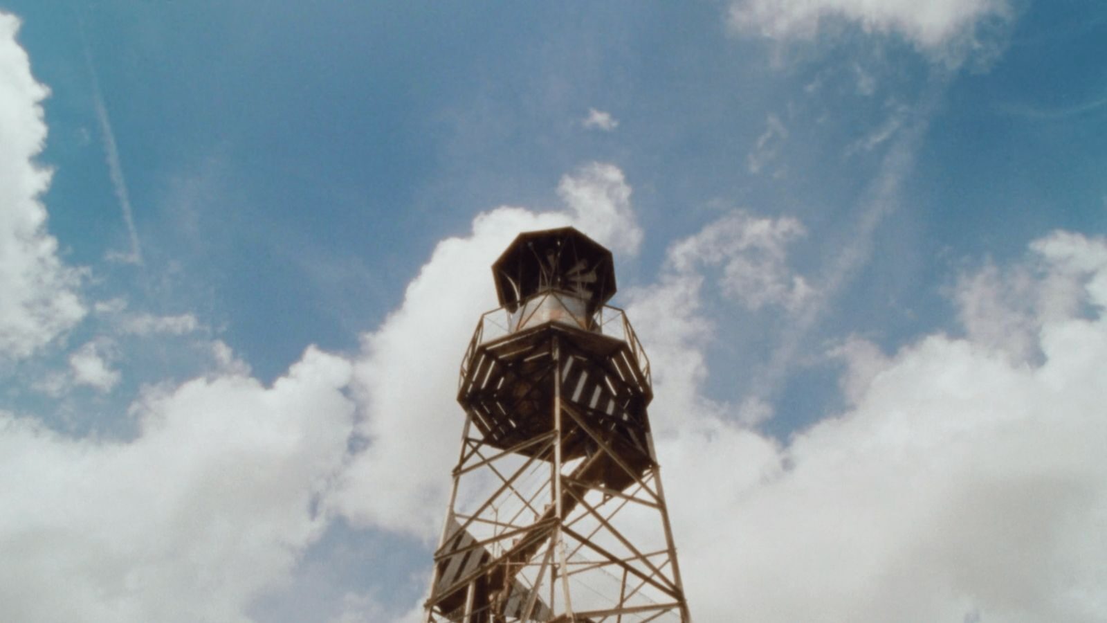 A metal tower against a blue sky and billowing clouds.